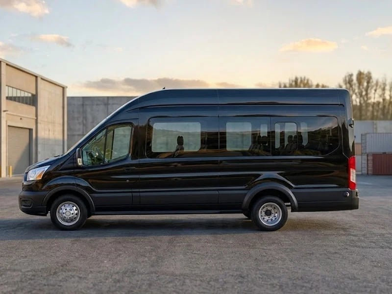 Black passenger van parked on a concrete surface with industrial buildings in the background